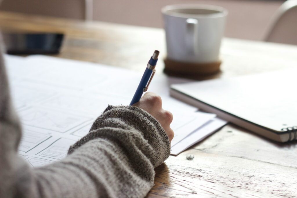person writing on brown wooden table near white ceramic mug reviewing RRSP documents