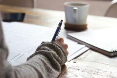 Photo by Unseen Studio person writing on brown wooden table near white ceramic mug